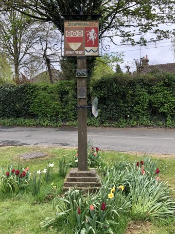 Fawkham Village sign on a wooden post with tulips and daffodils planted beneath