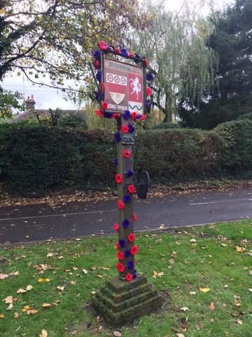 photo of village signpost decorated with red and purple poppies